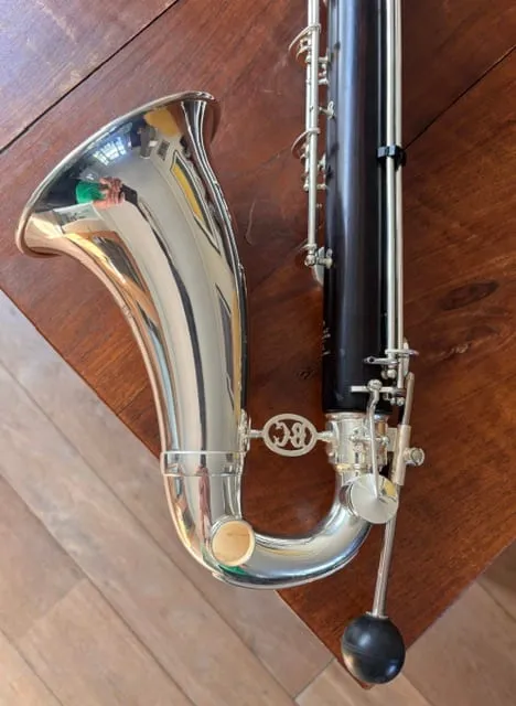 De zilveren beker van een basklarinet op een houten vloer