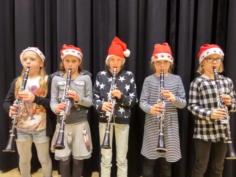 Vijf jonge klarinettisten met kerstmutsen spelen samen