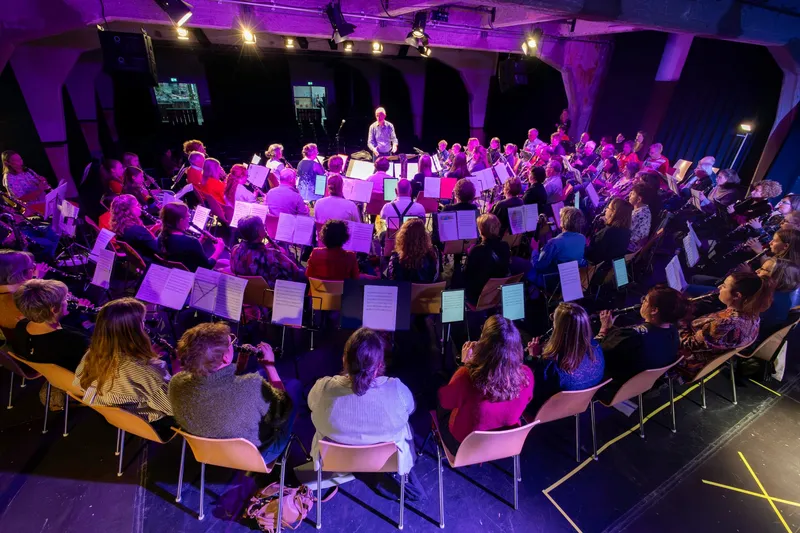 Een zaal vol klarinettisten repeteert samen in paars podiumlicht